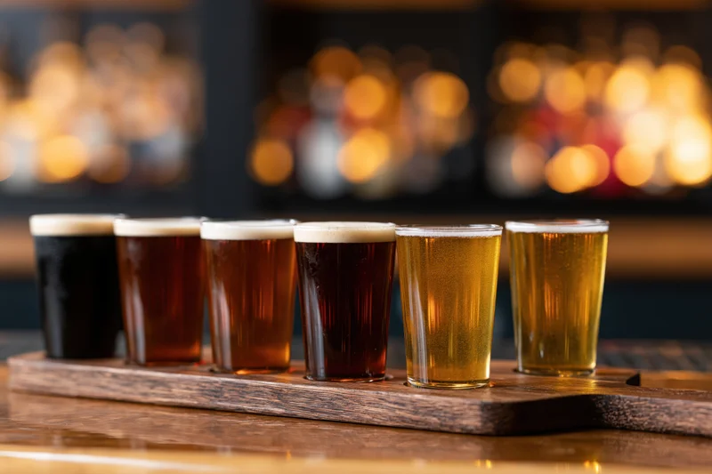 Six craft beer tasting flight glasses arranged in a row on a wooden tray at a bar