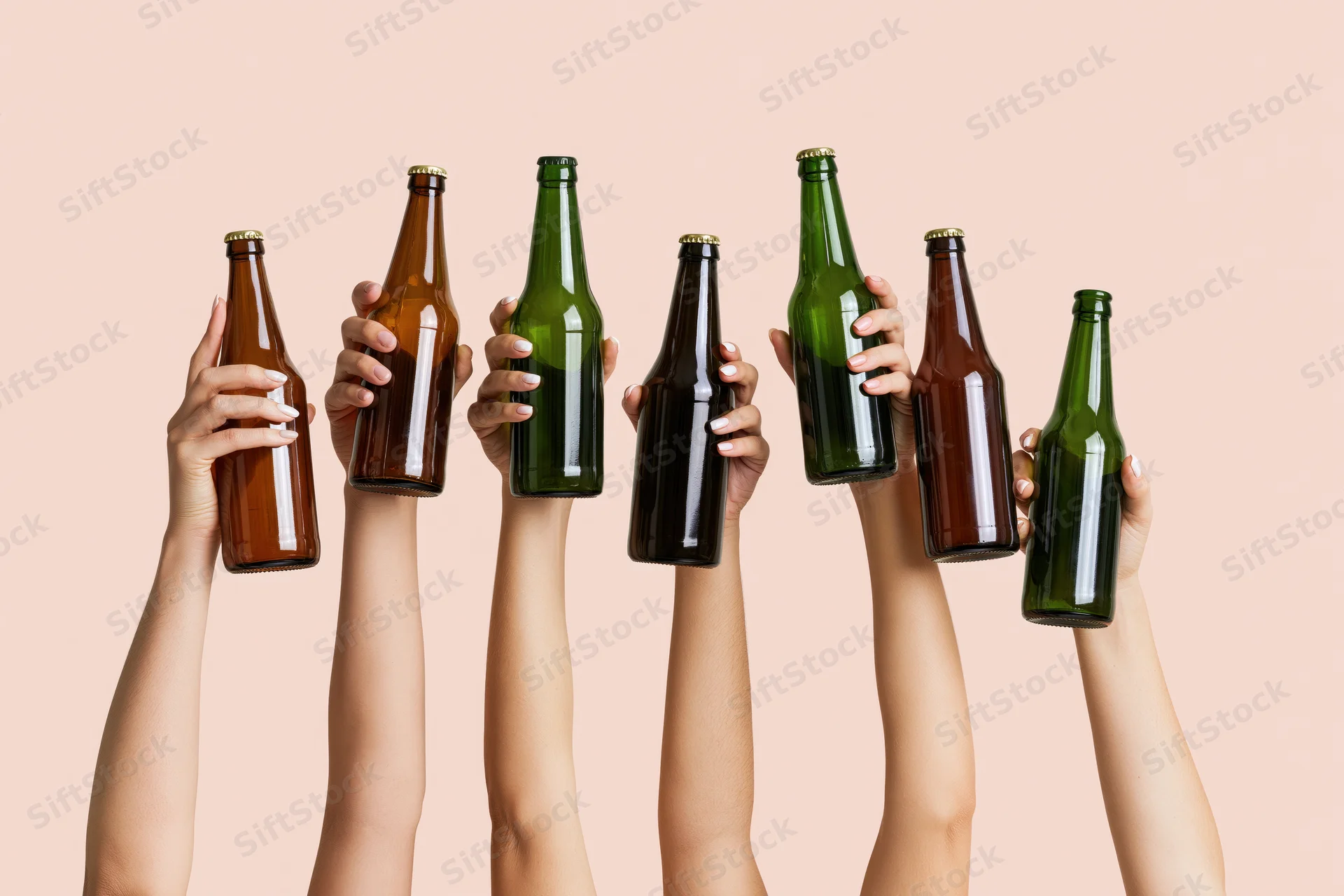 Six hands raised upward holding assorted glass beer bottles in the air