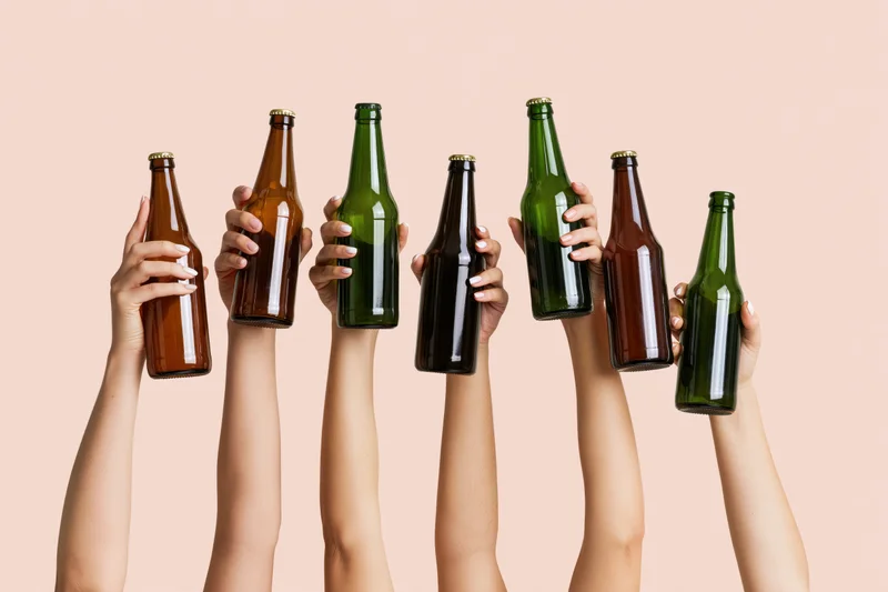 Six hands raised upward holding assorted glass beer bottles in the air