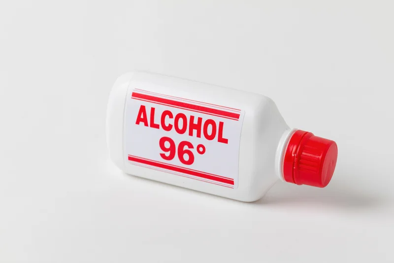 White plastic bottle of 96-degree rubbing alcohol lying on a plain white surface