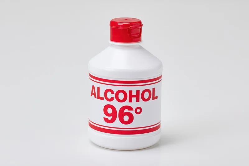 White plastic bottle of 96 degree rubbing alcohol with red cap and label on plain background