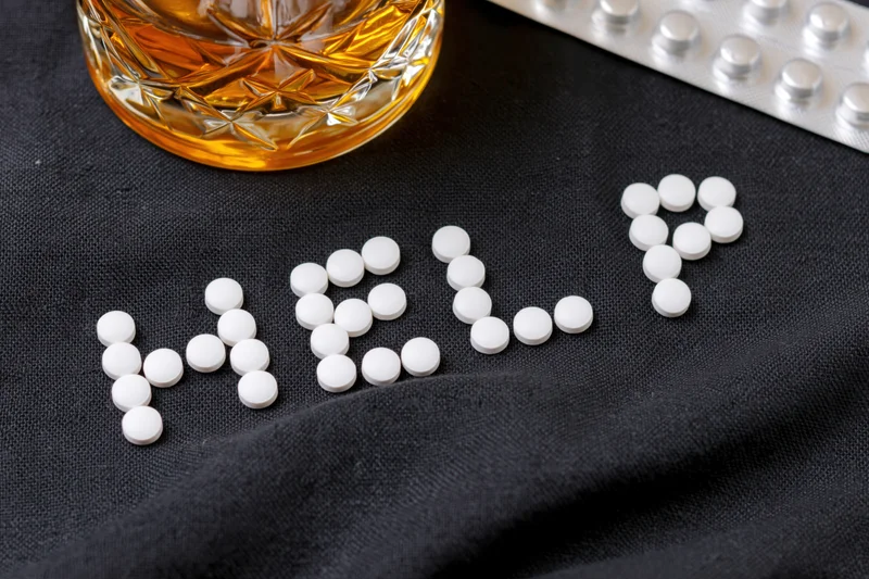 White pills arranged to spell help on black fabric beside a glass of whiskey