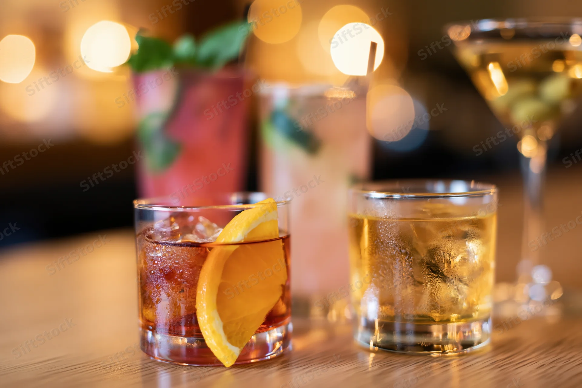 Three cocktails with garnishes arranged on a wooden bar top under warm ambient lighting