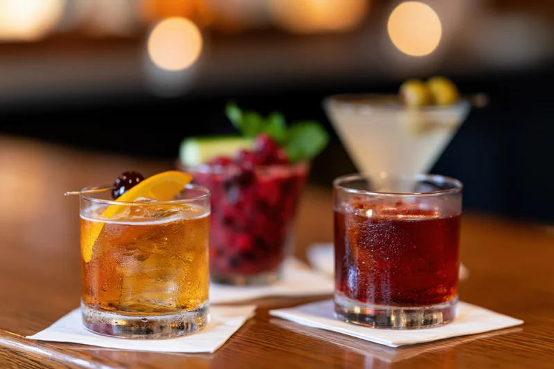 Three cocktails with garnishes arranged on a wooden bar top