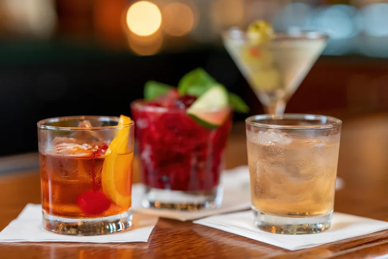 Four cocktails with garnishes arranged on a wooden bar top