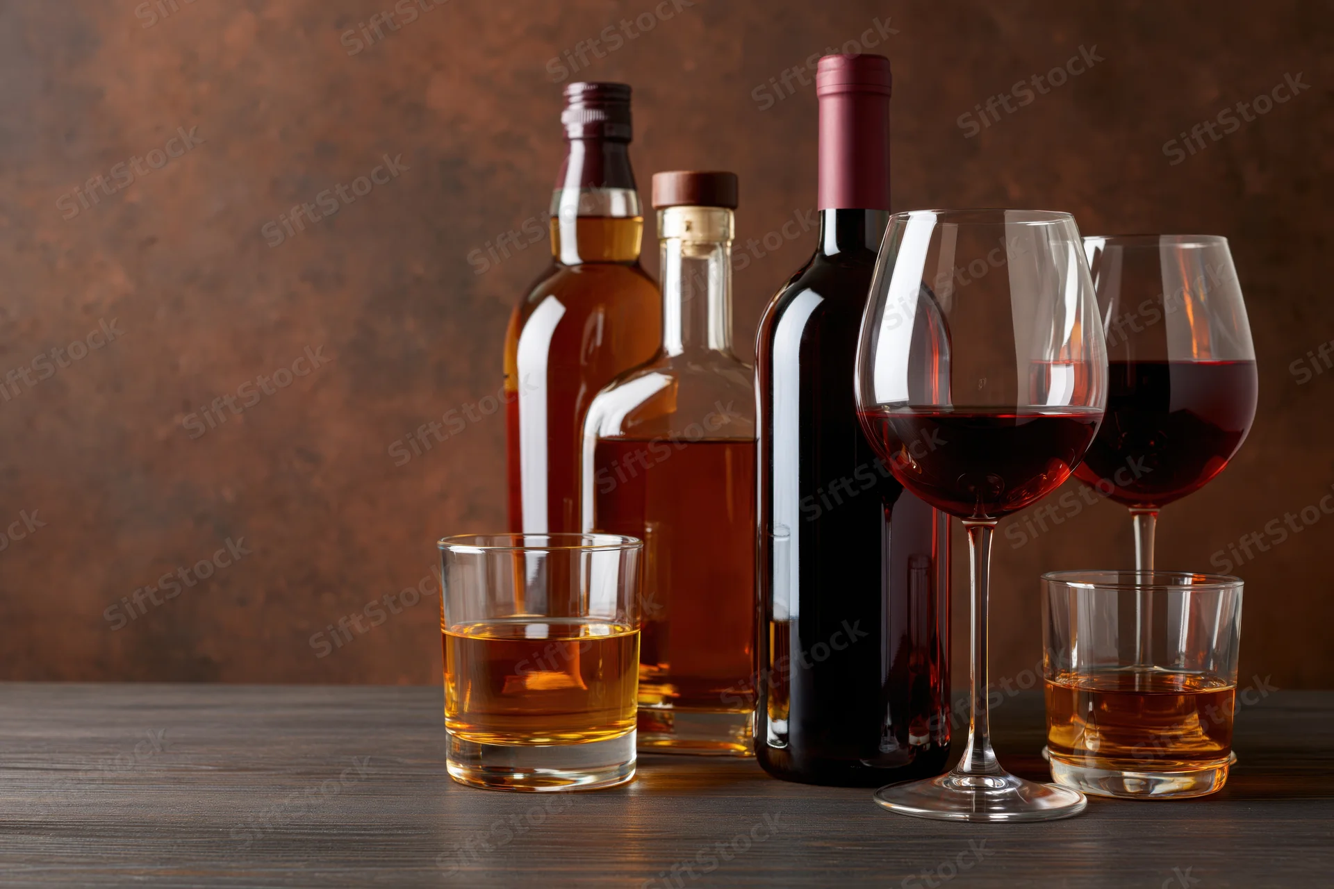 Whiskey and wine bottles with glasses arranged on a wooden table