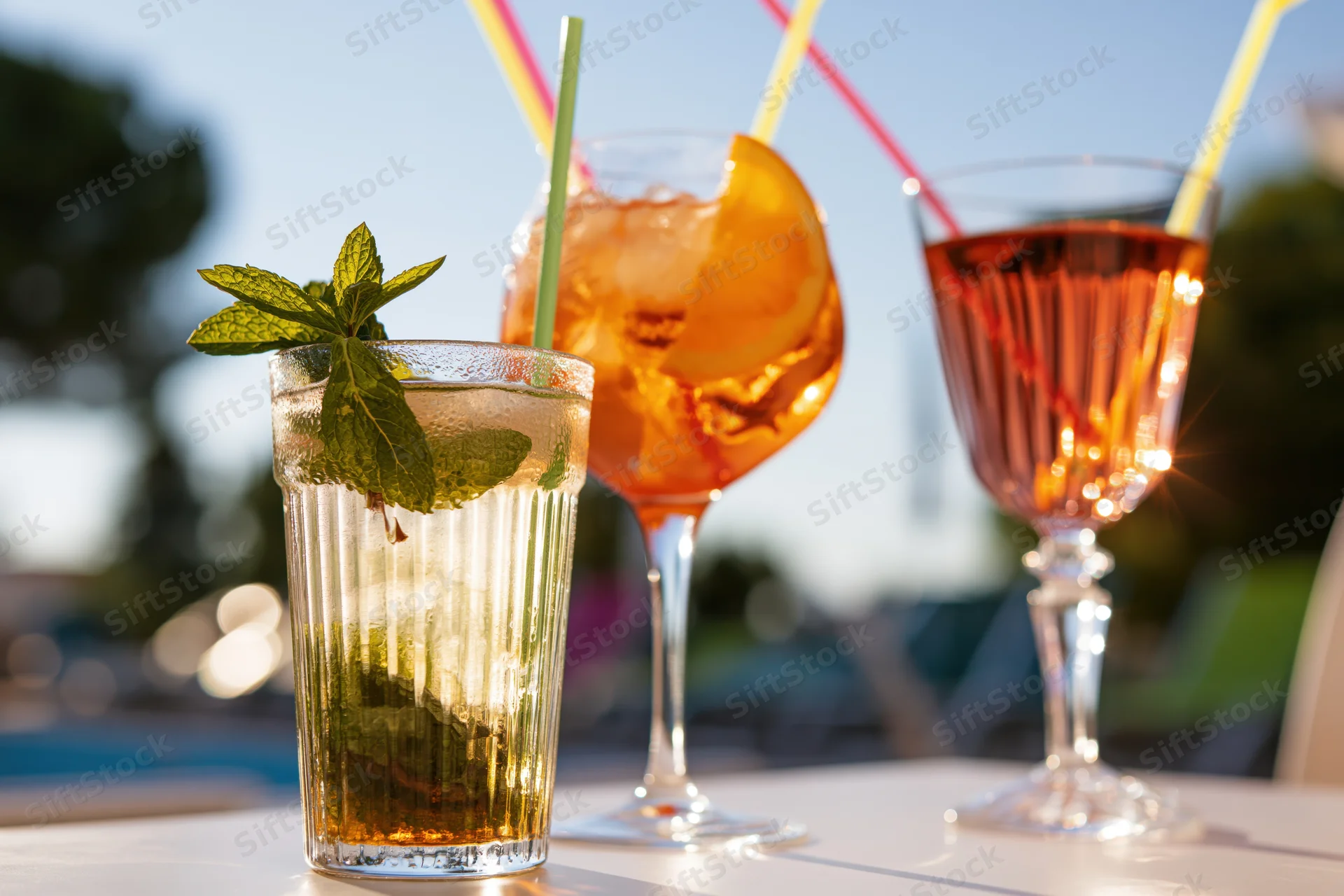 Three summer cocktails with mint, orange, and straws on an outdoor table