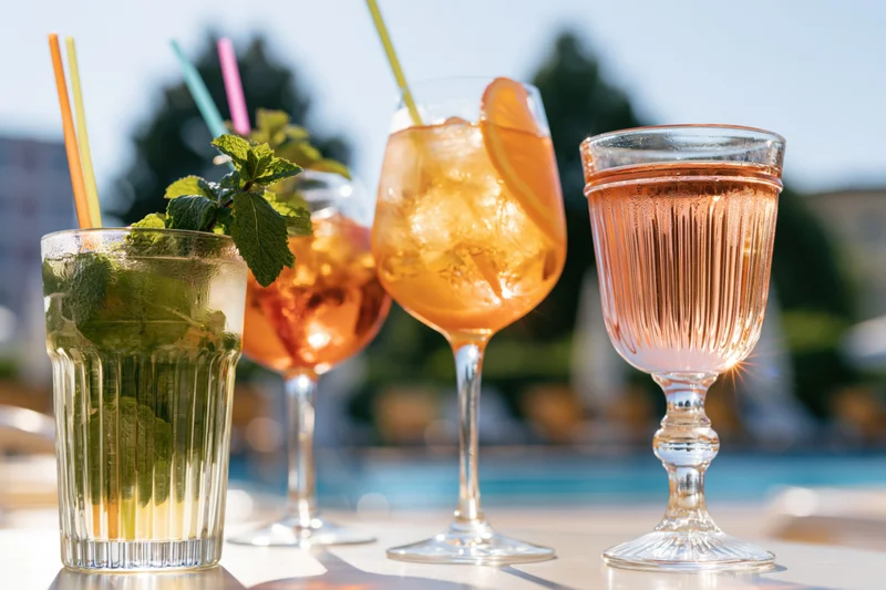Four summer cocktails with mint, citrus and straws on an outdoor table by a pool