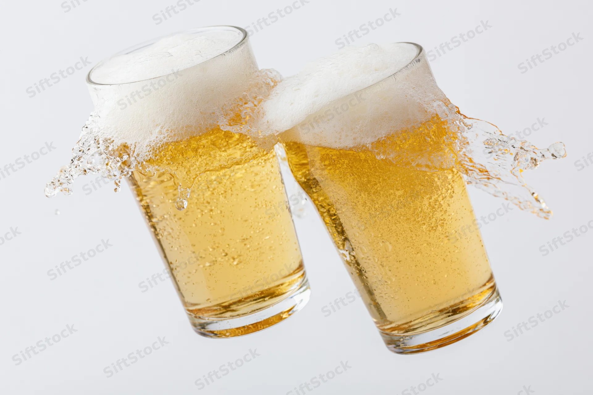 Two pint glasses of pale lager clinking with foam splashing against white background