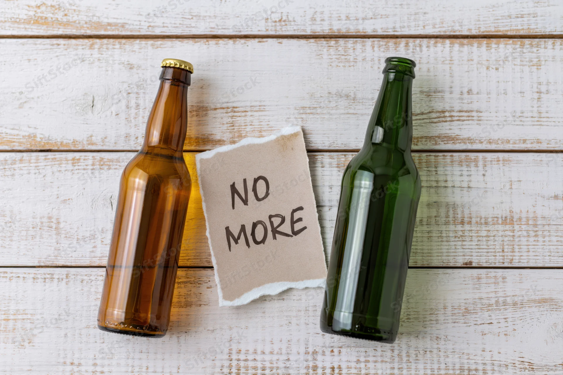 Two empty beer bottles and a note reading no more on whitewashed wood