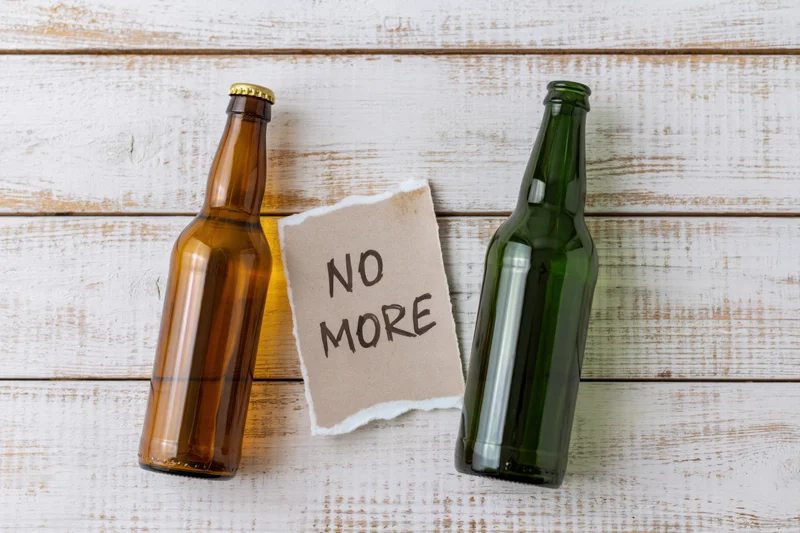 Two empty beer bottles and a note reading no more on whitewashed wood