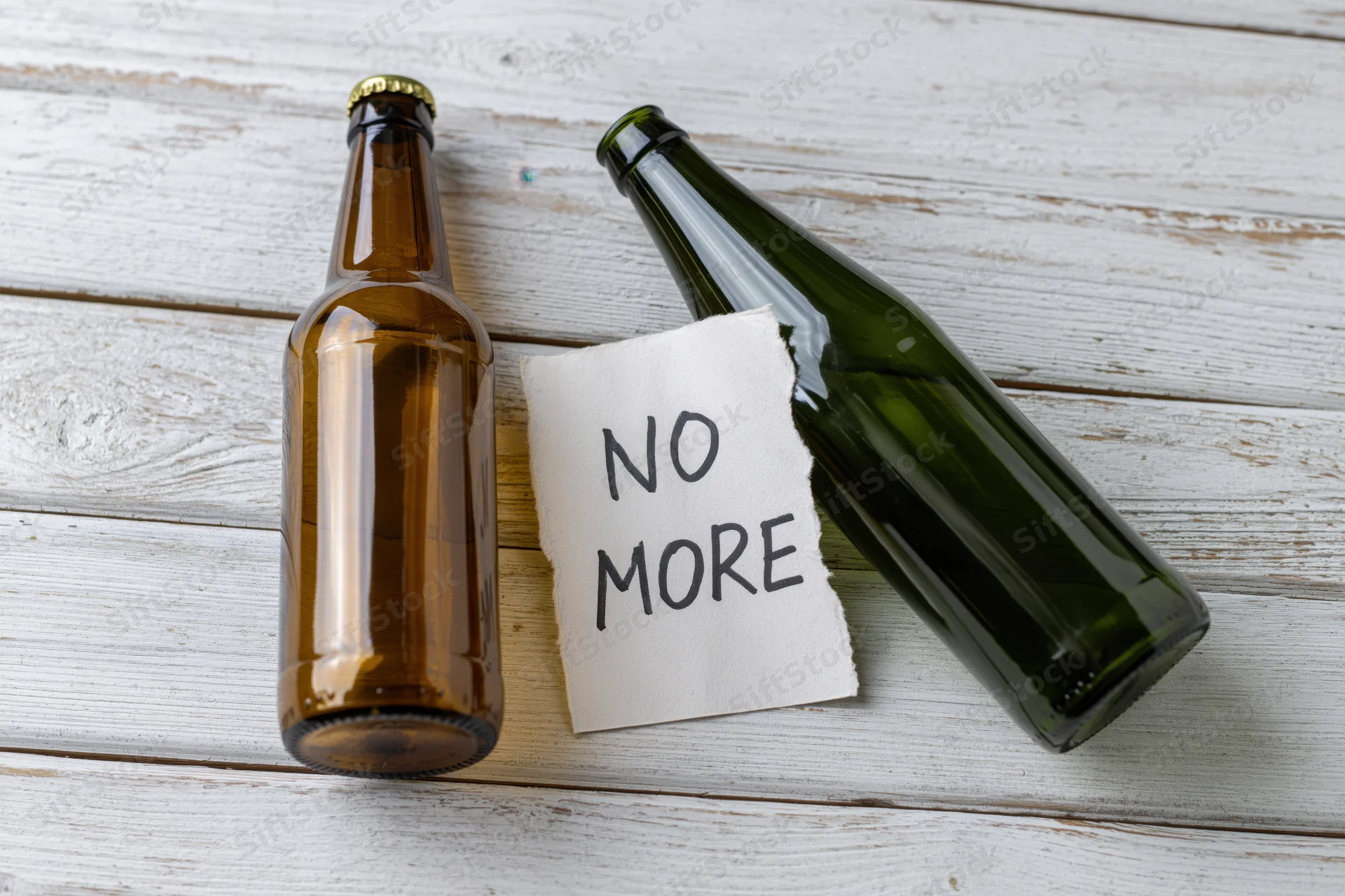 Two empty beer bottles and a note reading no more on a whitewashed wooden surface