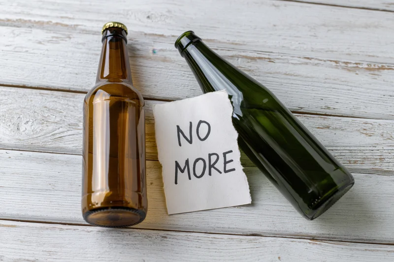 Two empty beer bottles and a note reading no more on a whitewashed wooden surface