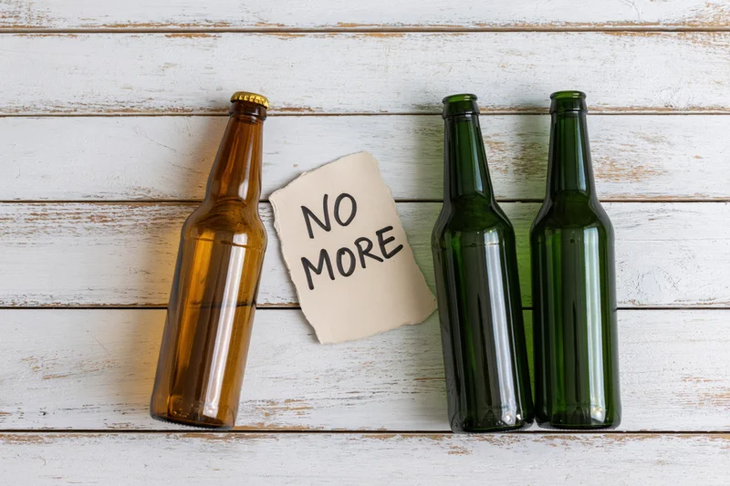 Empty beer bottles and a note reading no more on whitewashed wood