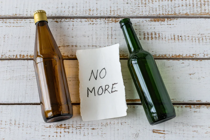 Two empty beer bottles and a handwritten note reading no more on whitewashed wooden planks