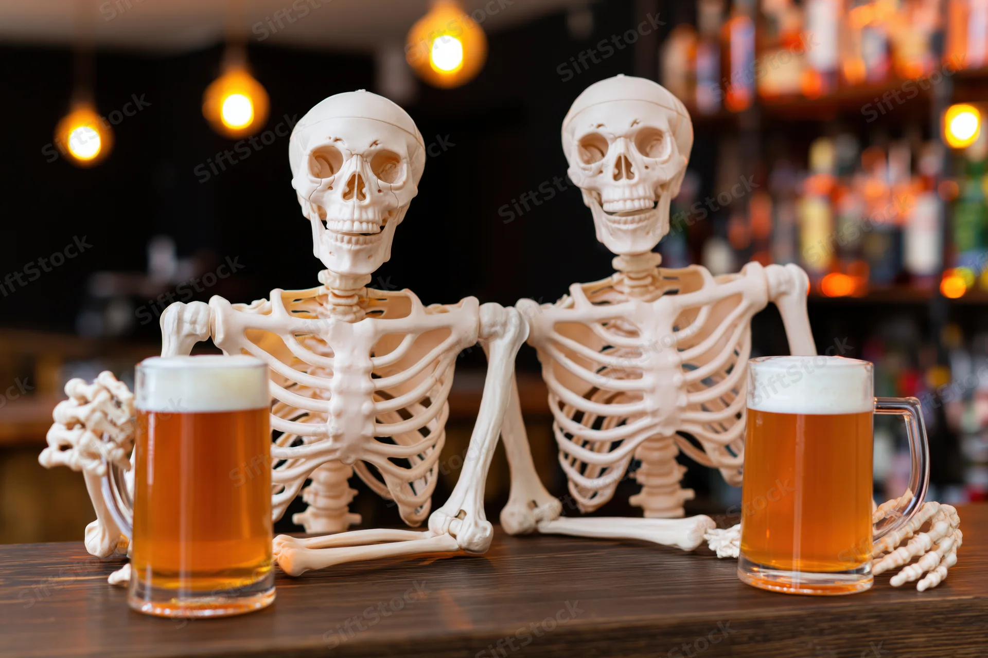 Two plastic skeletons sitting side by side at a wooden bar counter with beer mugs in front of them