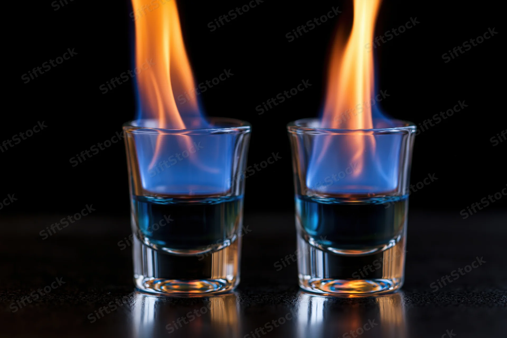 Two shot glasses with burning blue liquid flames on a dark surface