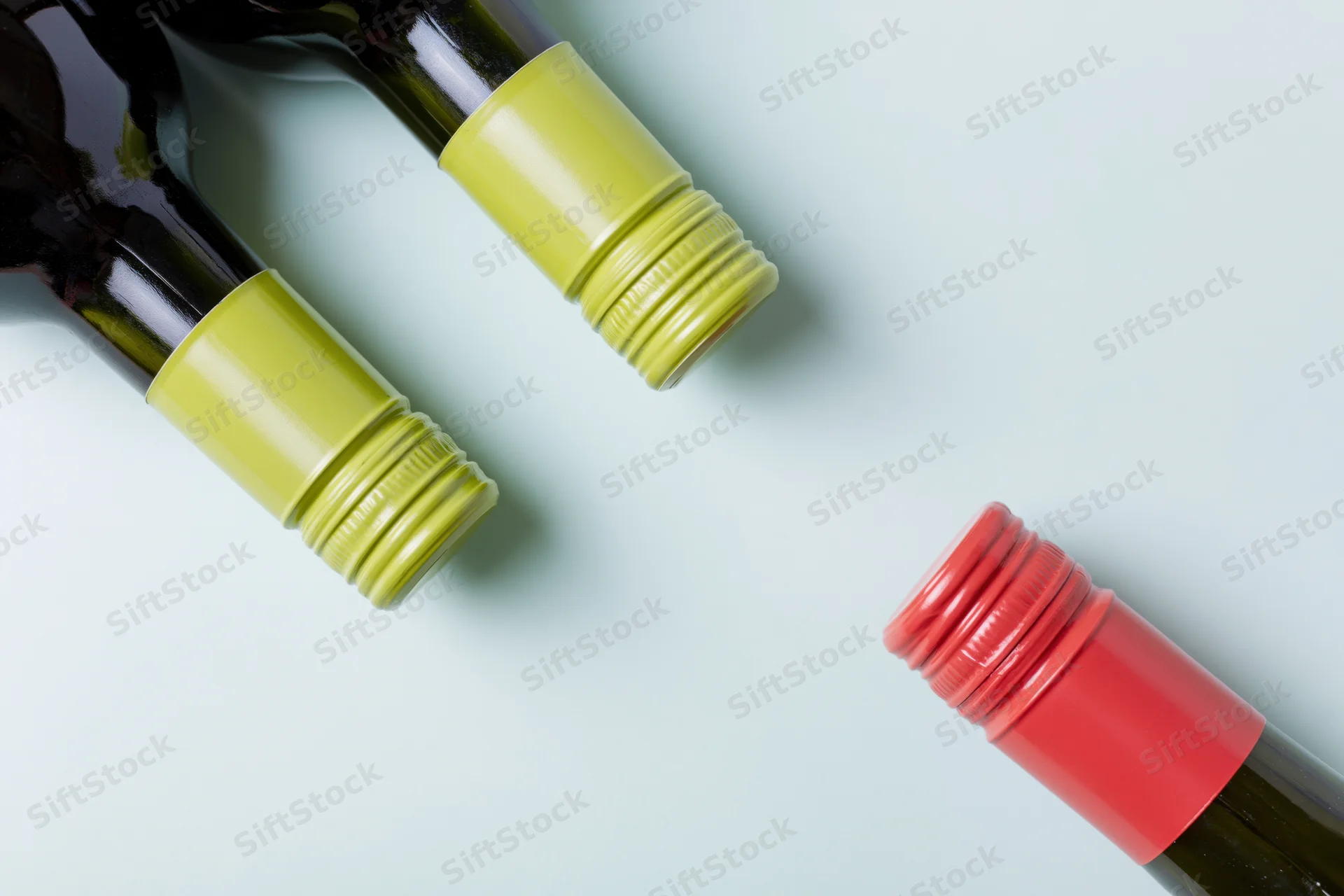 Three wine bottles lying flat on a light blue surface with caps visible, cropped at necks