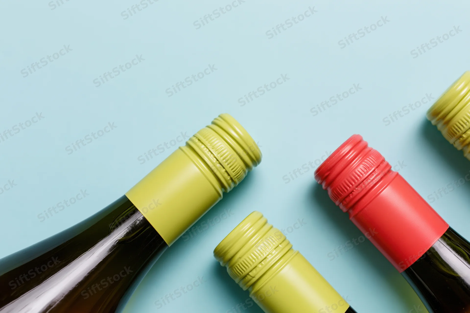 Wine bottles lying flat on a blue background with yellow and red caps, top view