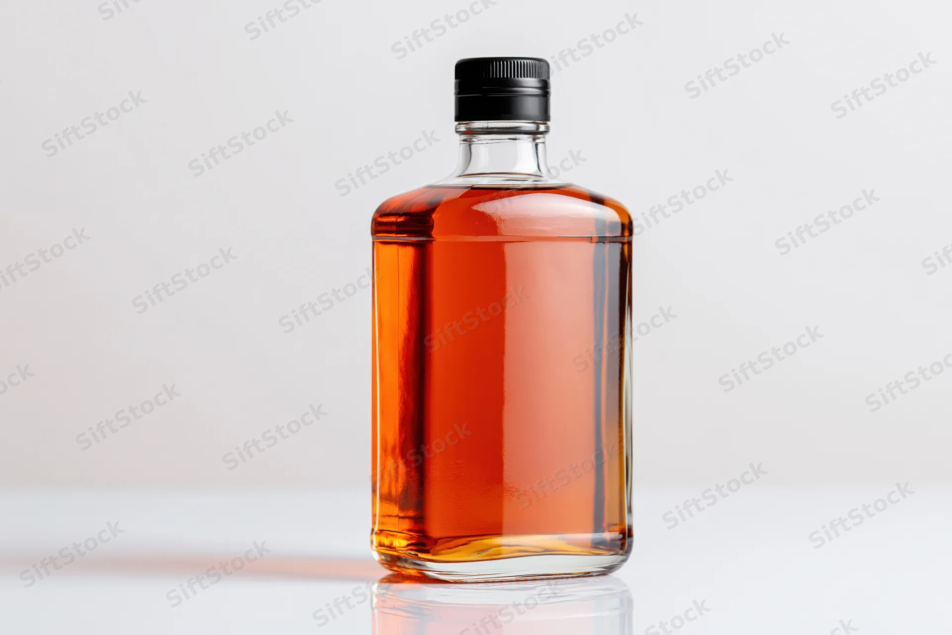 Clear glass whiskey bottle filled with amber liquid on white surface