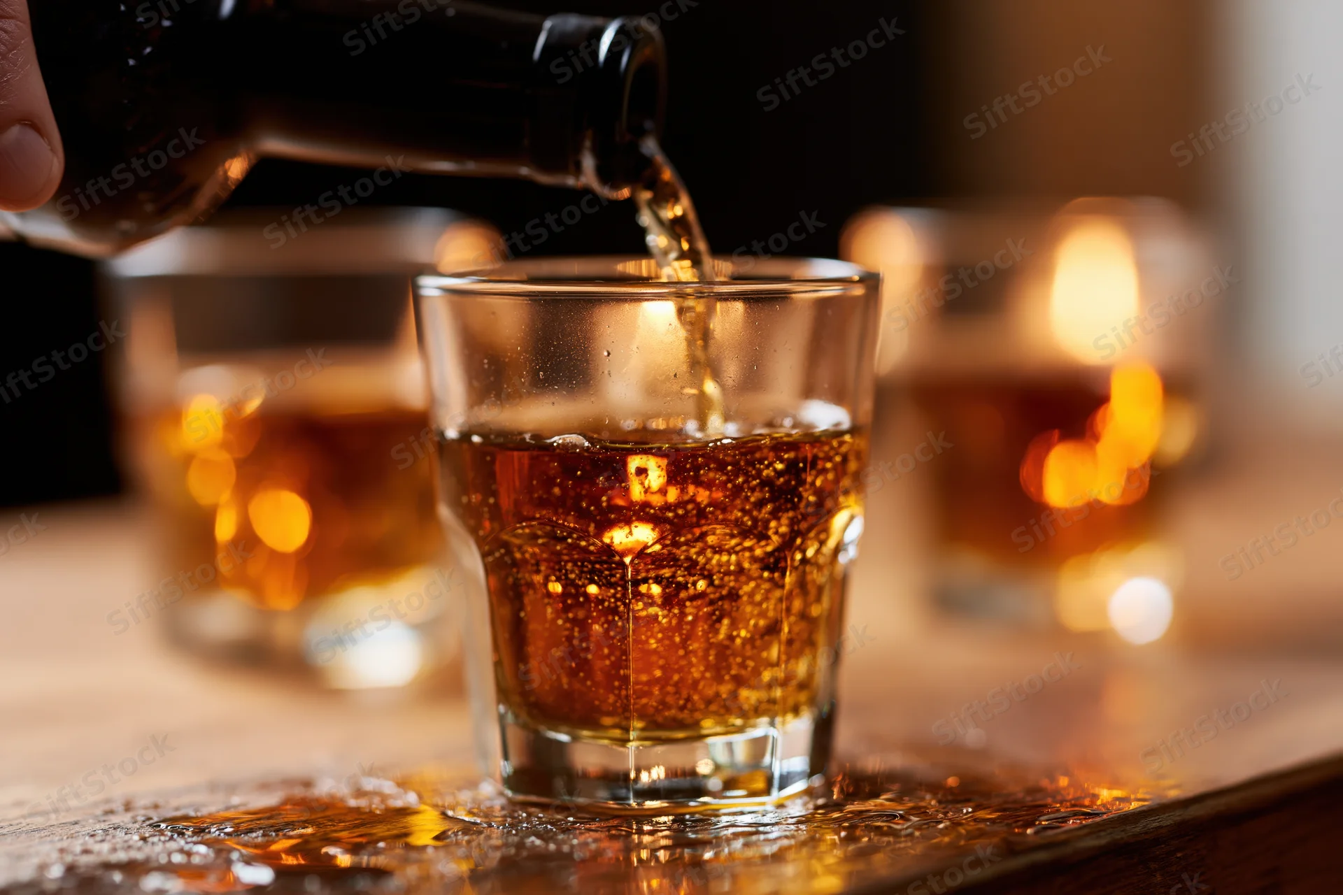 Whiskey being poured from a dark bottle into a rocks glass on a wooden bar surface