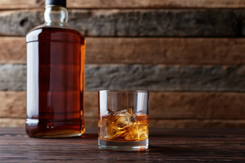 Whiskey bottle and rocks glass with ice on a wooden table