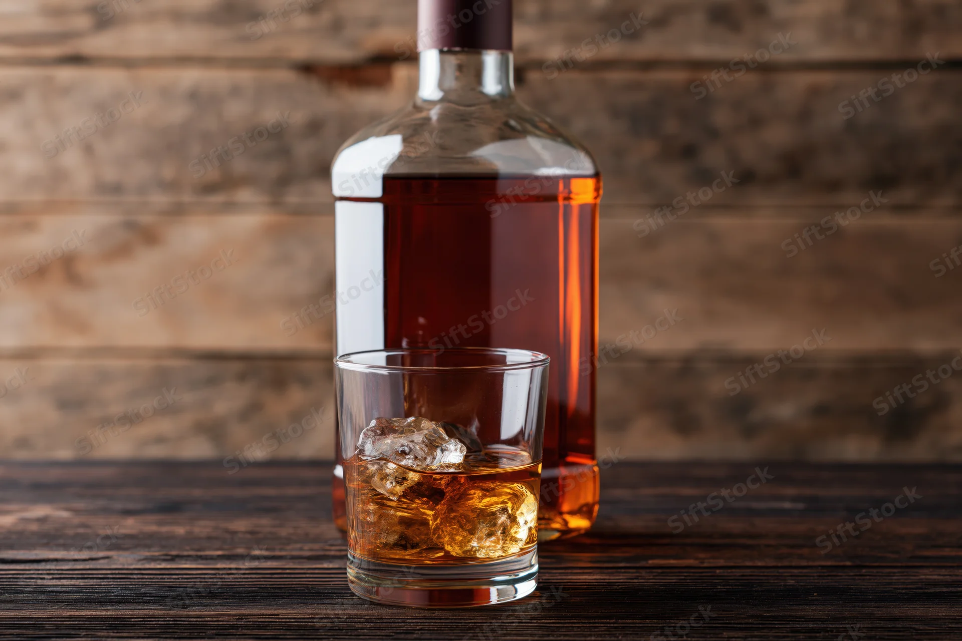Whiskey bottle and rocks glass with ice on wooden table