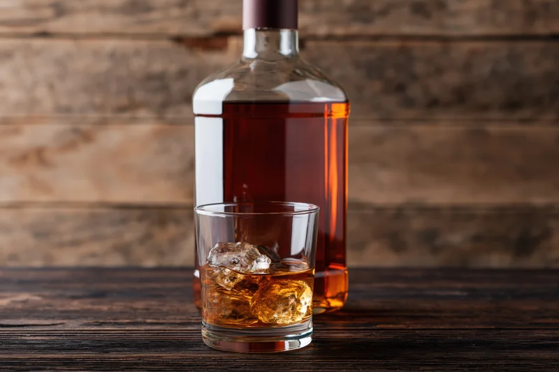 Whiskey bottle and rocks glass with ice on wooden table