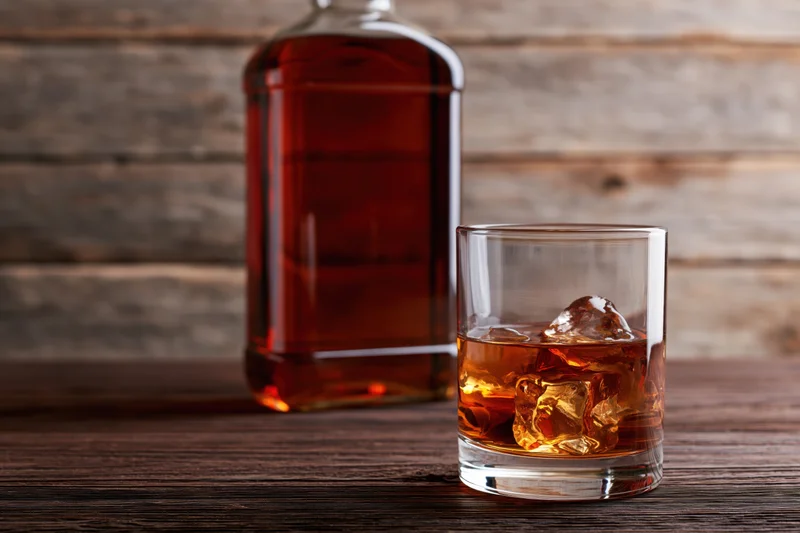 Whiskey bottle and rocks glass with ice on wooden table