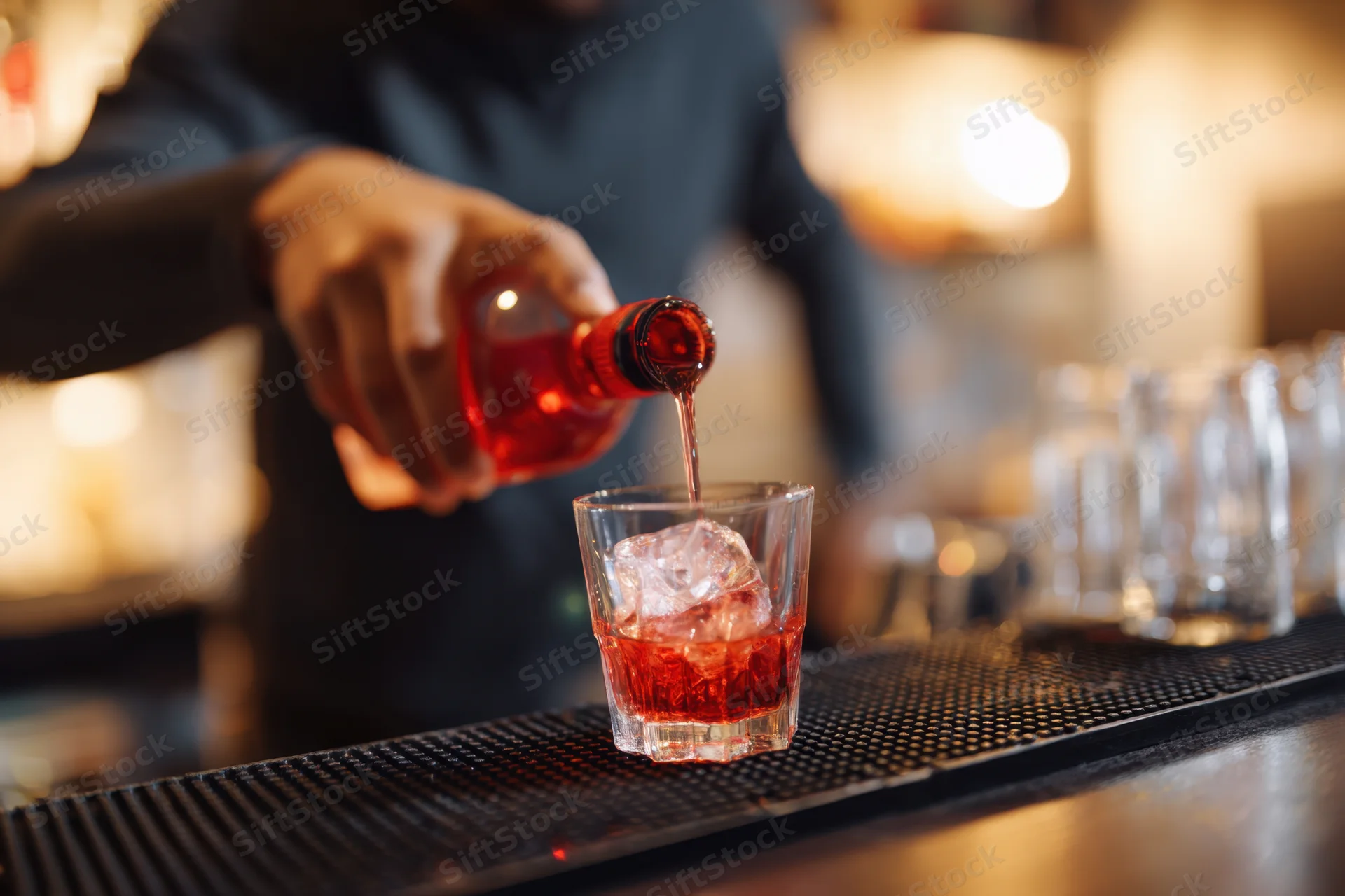 Bartender pouring red liquor into a glass with ice on a bar counter