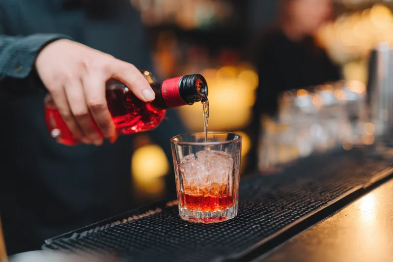 Bartender pouring red liquor into a glass with ice on a bar counter