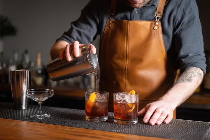 Bartender pouring cocktails into glasses on a bar counter