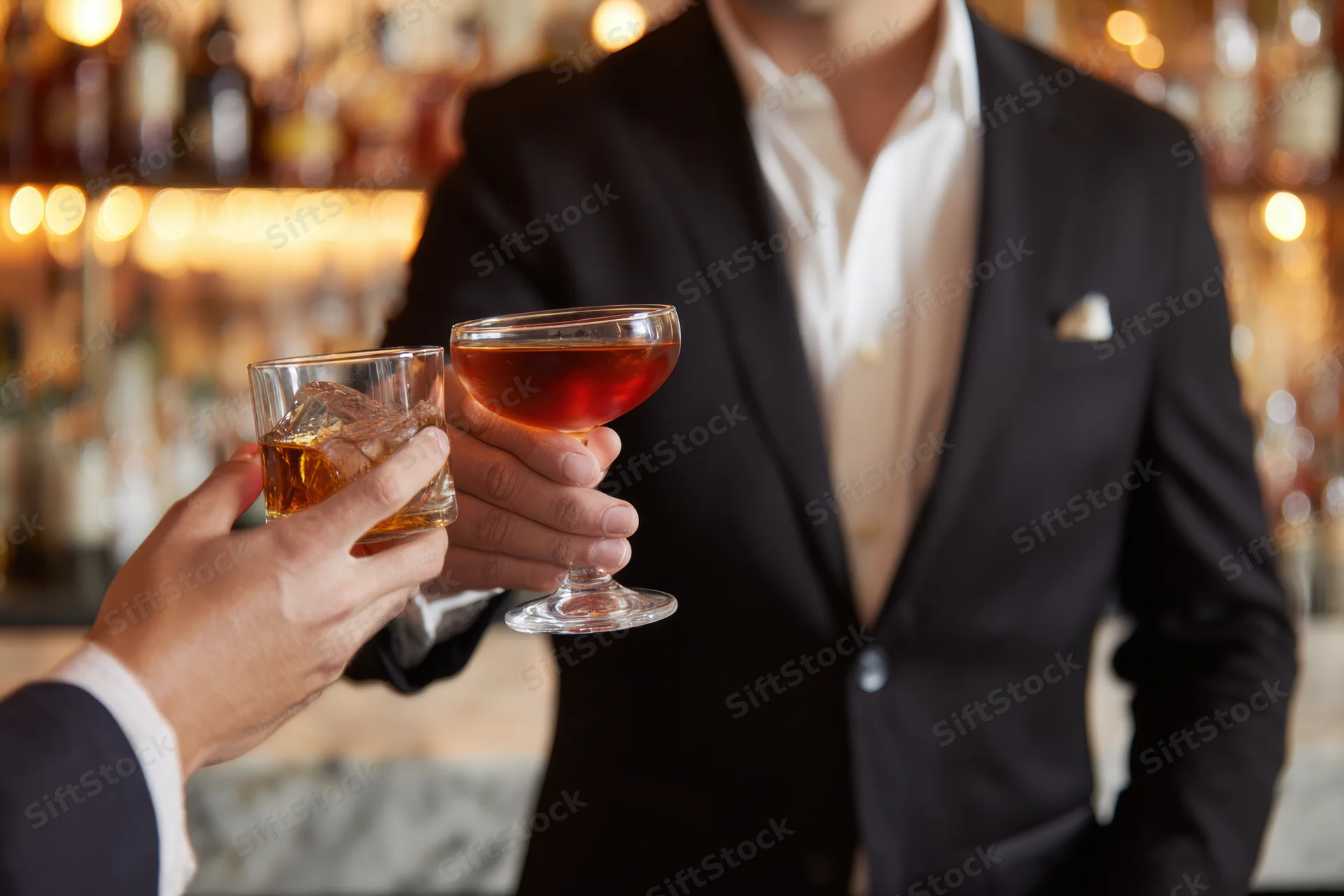 Man in black suit toasting with cocktail glass at bar
