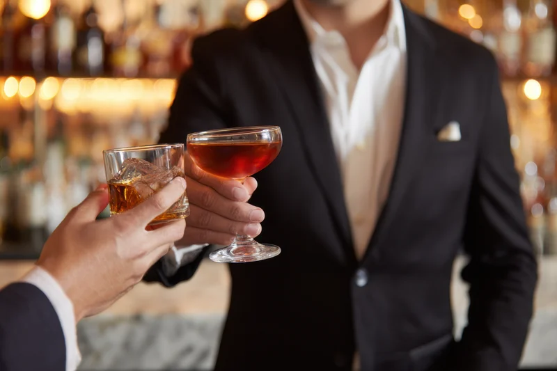 Man in black suit toasting with cocktail glass at bar