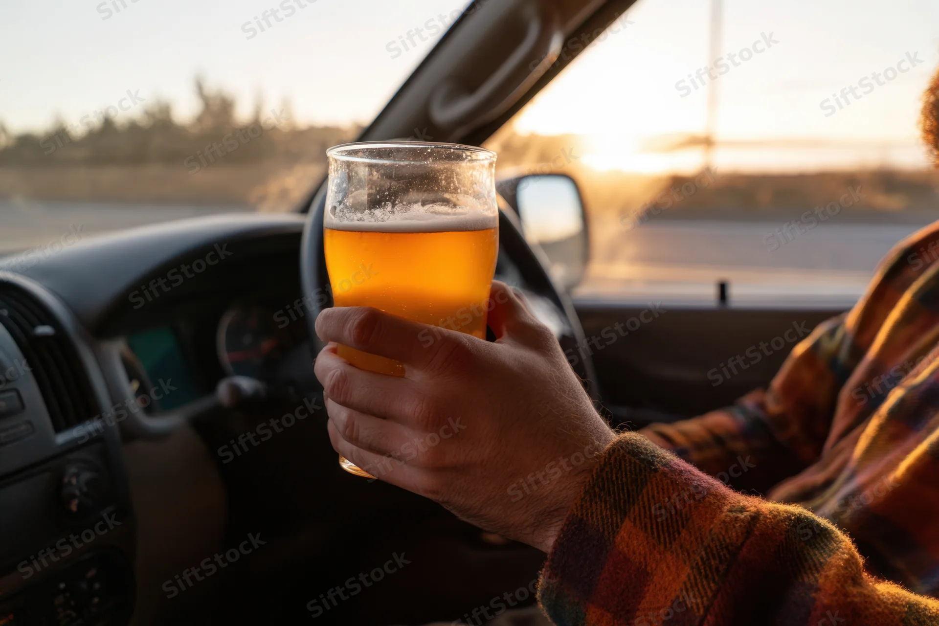 Hand holding a glass of beer inside a car during sunset