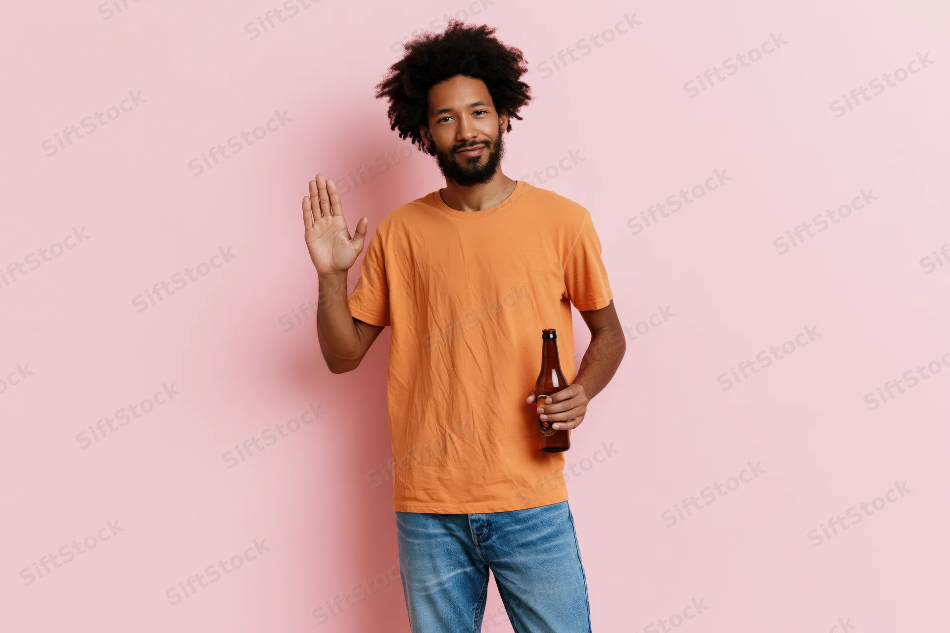 Young man in orange tshirt and jeans waving while holding a beer bottle against pink background