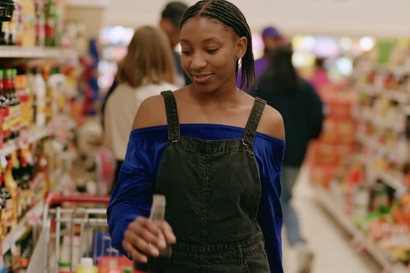 Young woman holding a soda bottle in a supermarket aisle, browsing products on shelves