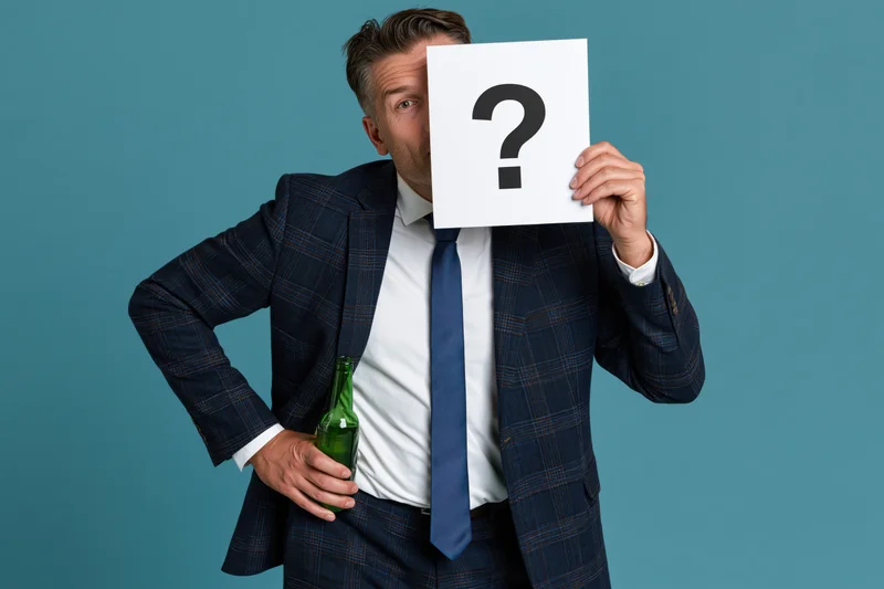 Man in suit holding question mark sign and green bottle in studio