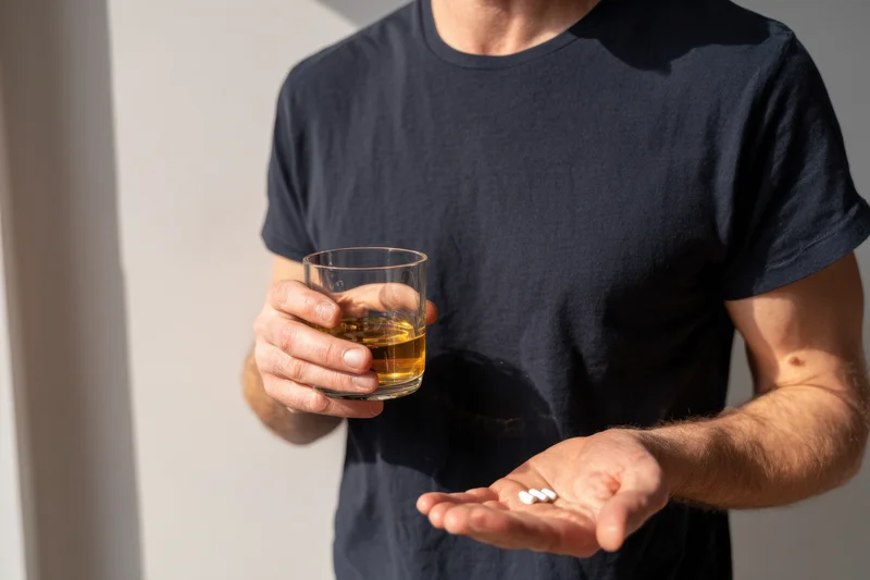 Man holding pills and a glass of whiskey in his hands indoors
