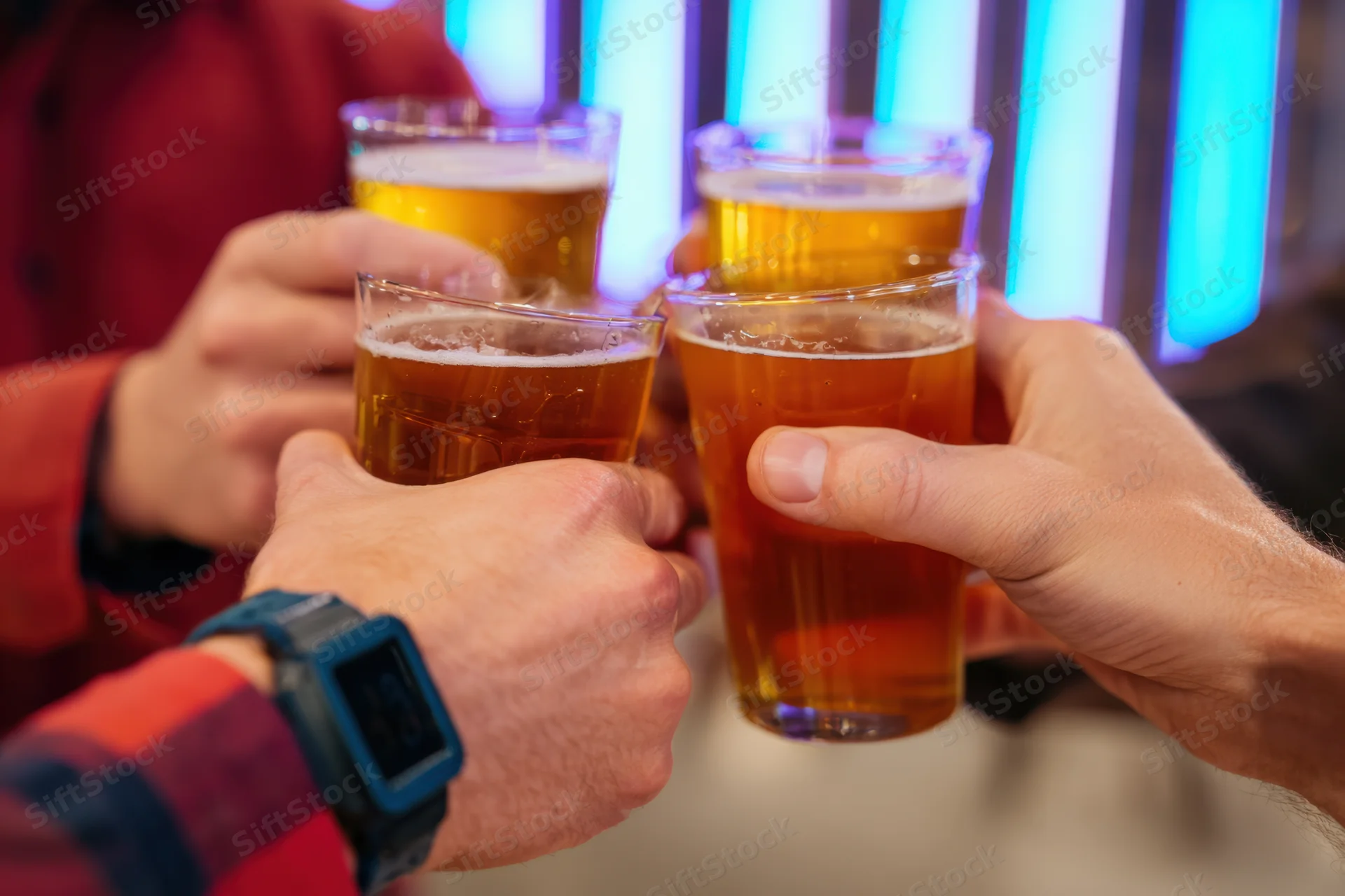 Multiple hands clinking beer glasses in a toast at a neon-lit bar