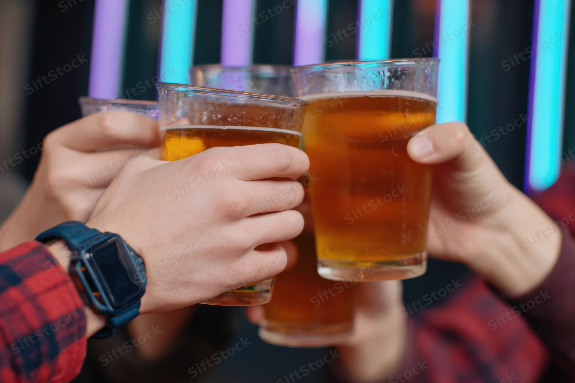 Multiple hands clinking beer glasses in a toast at a neon-lit bar