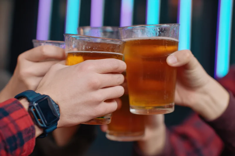 Multiple hands clinking beer glasses in a toast at a neon-lit bar