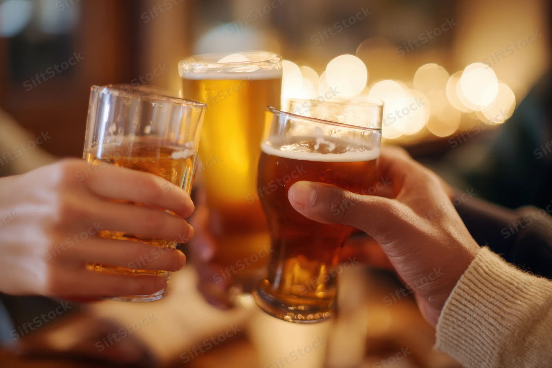 Multiple hands clinking beer glasses in a toast at a dimly lit bar