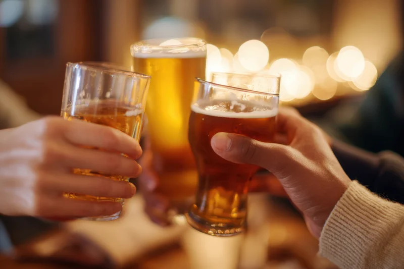 Multiple hands clinking beer glasses in a toast at a dimly lit bar