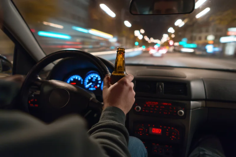 Driver holding beer bottle while driving at night in city traffic
