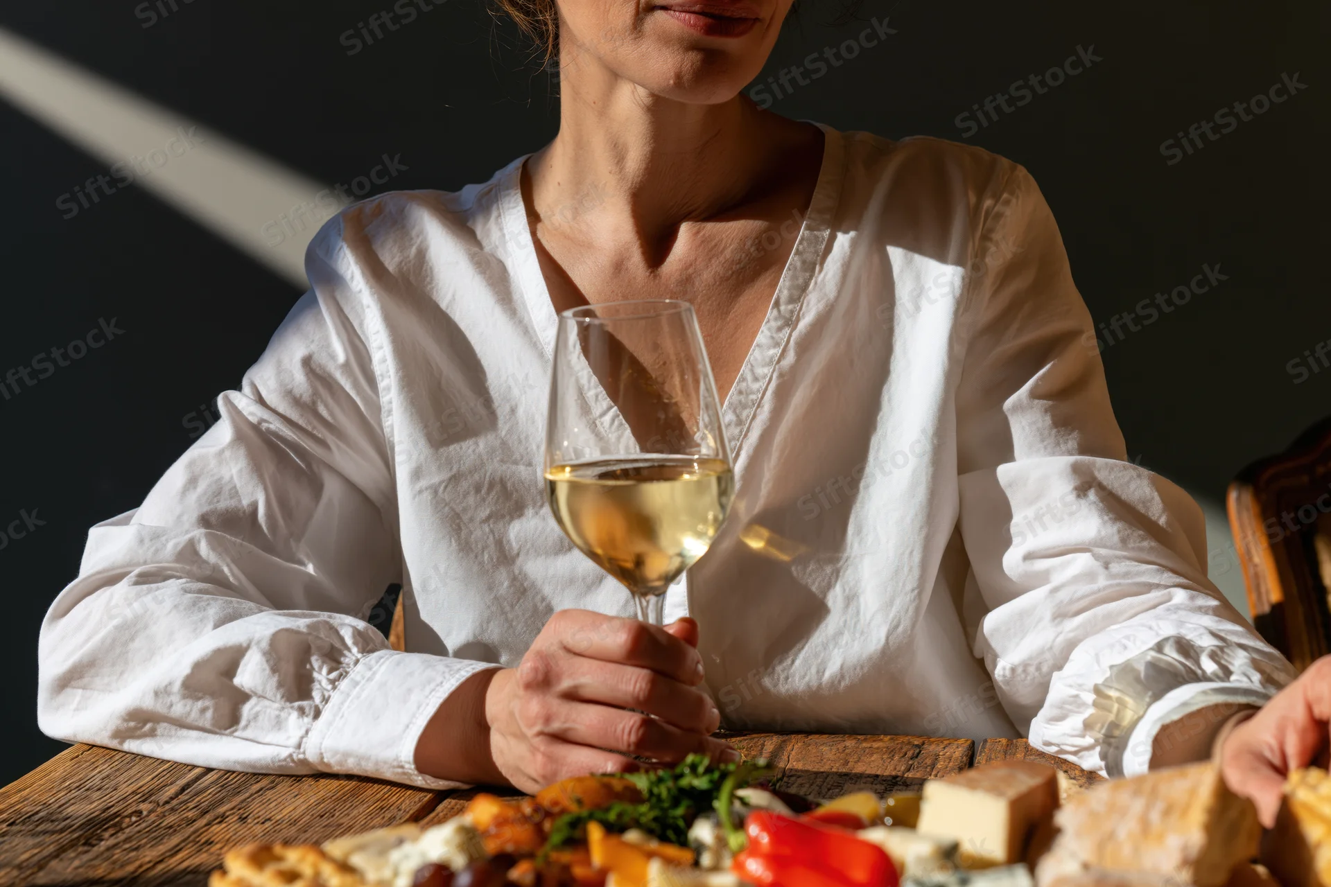 Woman holding wine glass at wooden table with charcuterie board