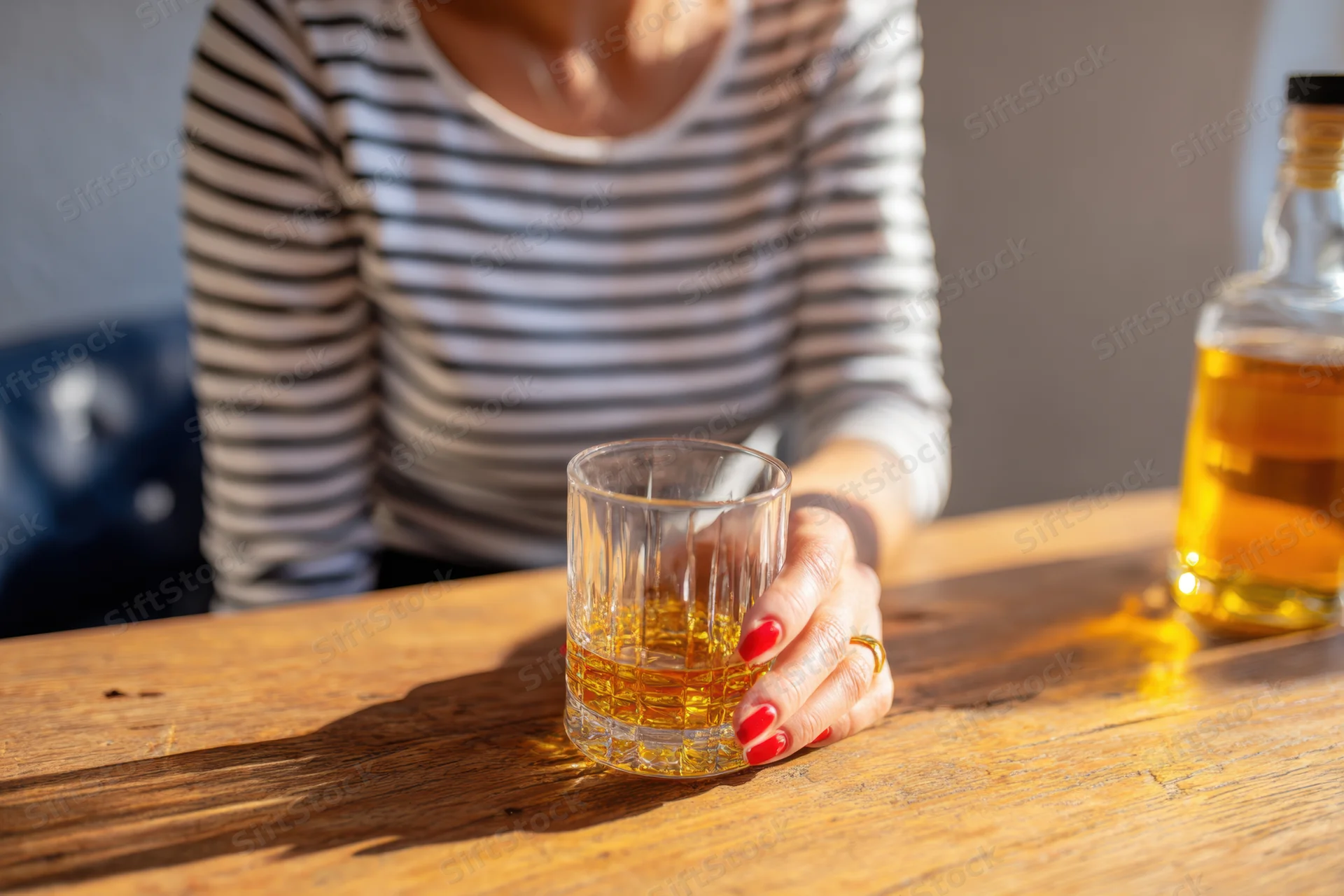 Woman holding a whiskey glass on a wooden table in a bar