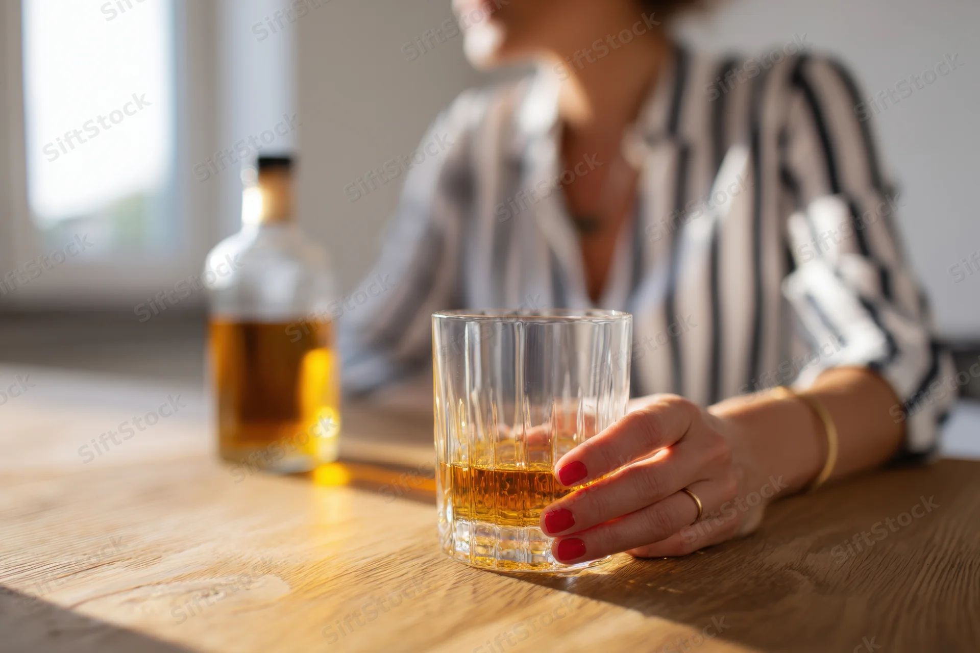 Woman holding a glass of whiskey on a wooden table indoors