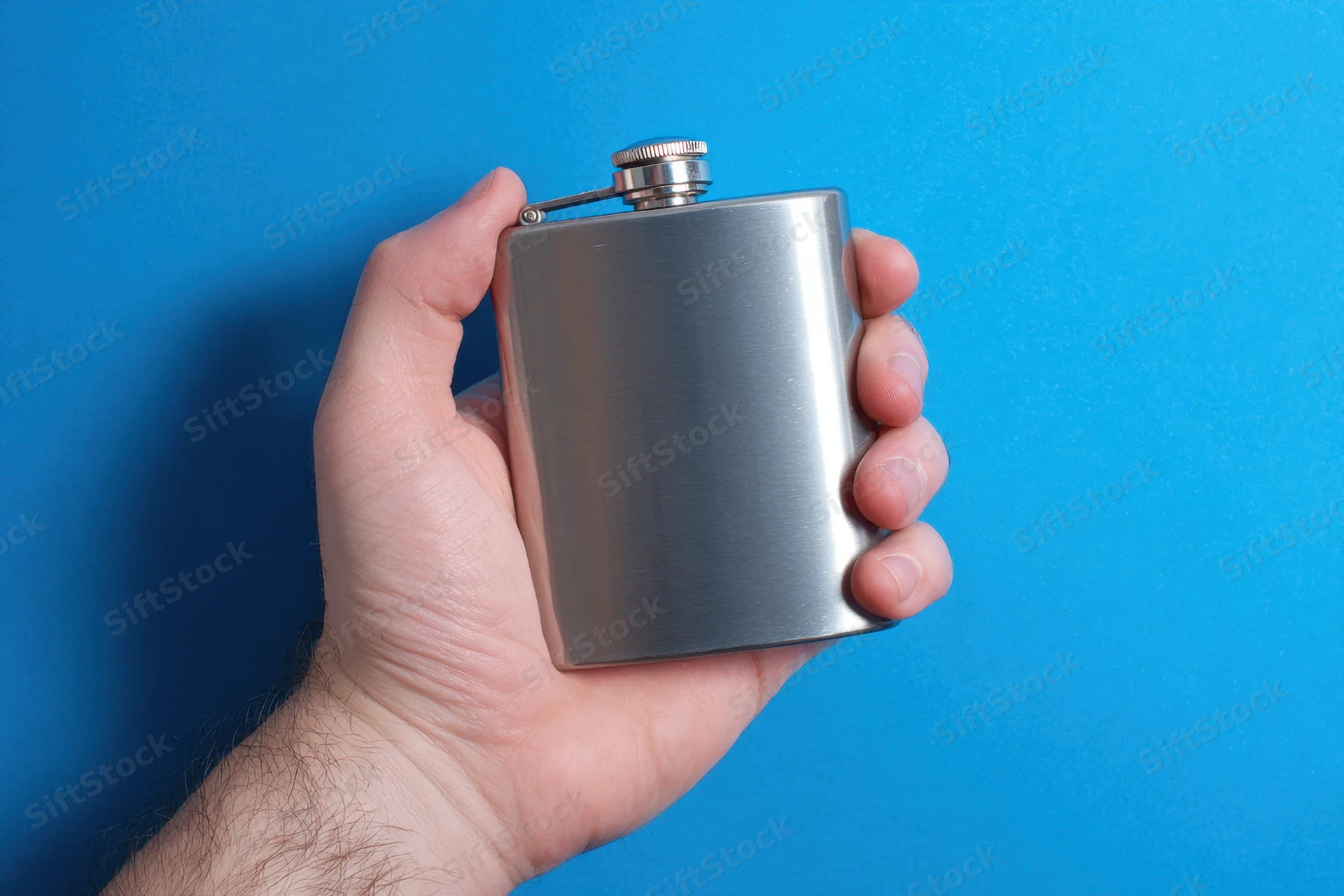 Hand gripping a brushed metal flask against a blue background