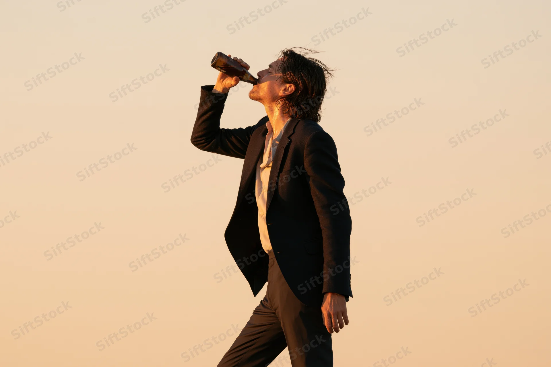 Man in dark blazer drinking beer outdoors at sunset